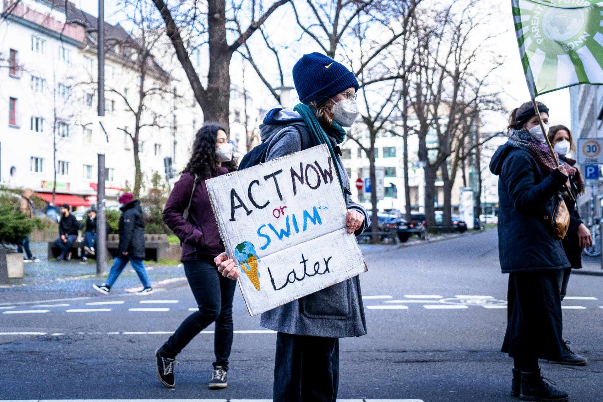 person holding a sign that says act now or swim later