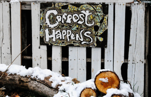 sign that says compost happens over snow covered logs