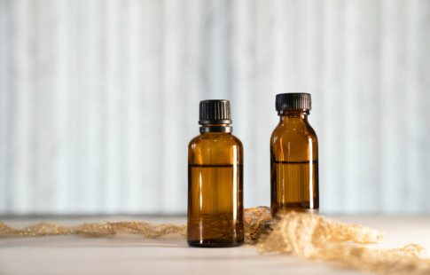 two amber bottles with liquid against white curtain