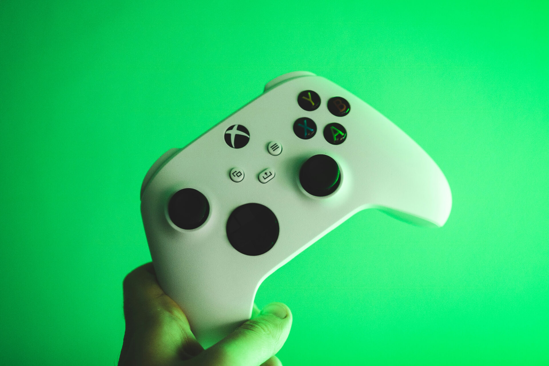 green Xbox controller held by a hand on green background