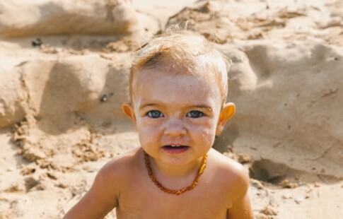 A baby sitting in the sand with sunscreen on its face.
