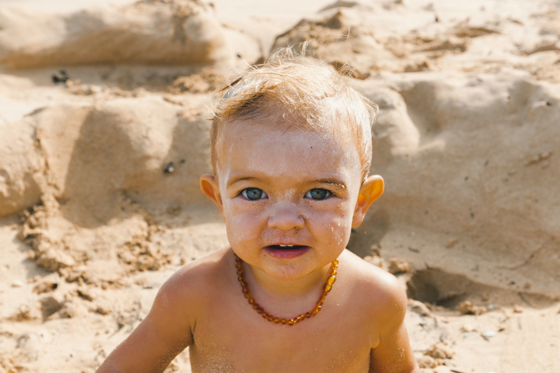 A baby sitting in the sand with sunscreen on its face.