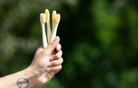 person with a peace sign tattoo on their wrist holding bamboo toothbrushes