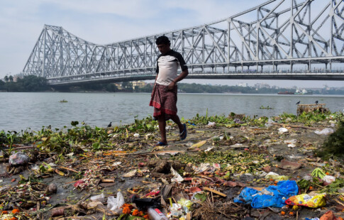 Man walks on a polluted riverbank.