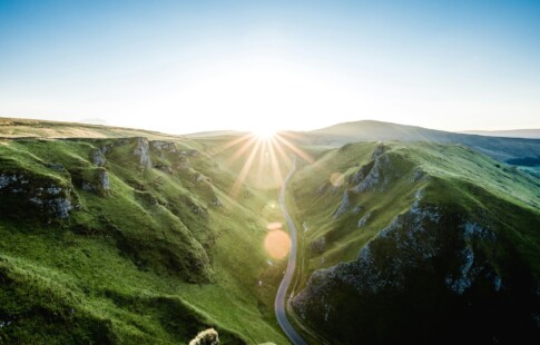 A mountain range with the sun over it and a blue sky