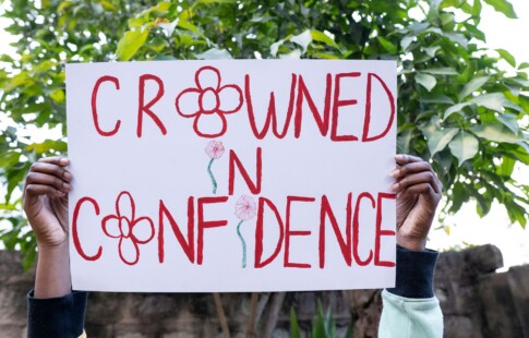 person holding sign saying crowned in confidence with flowers